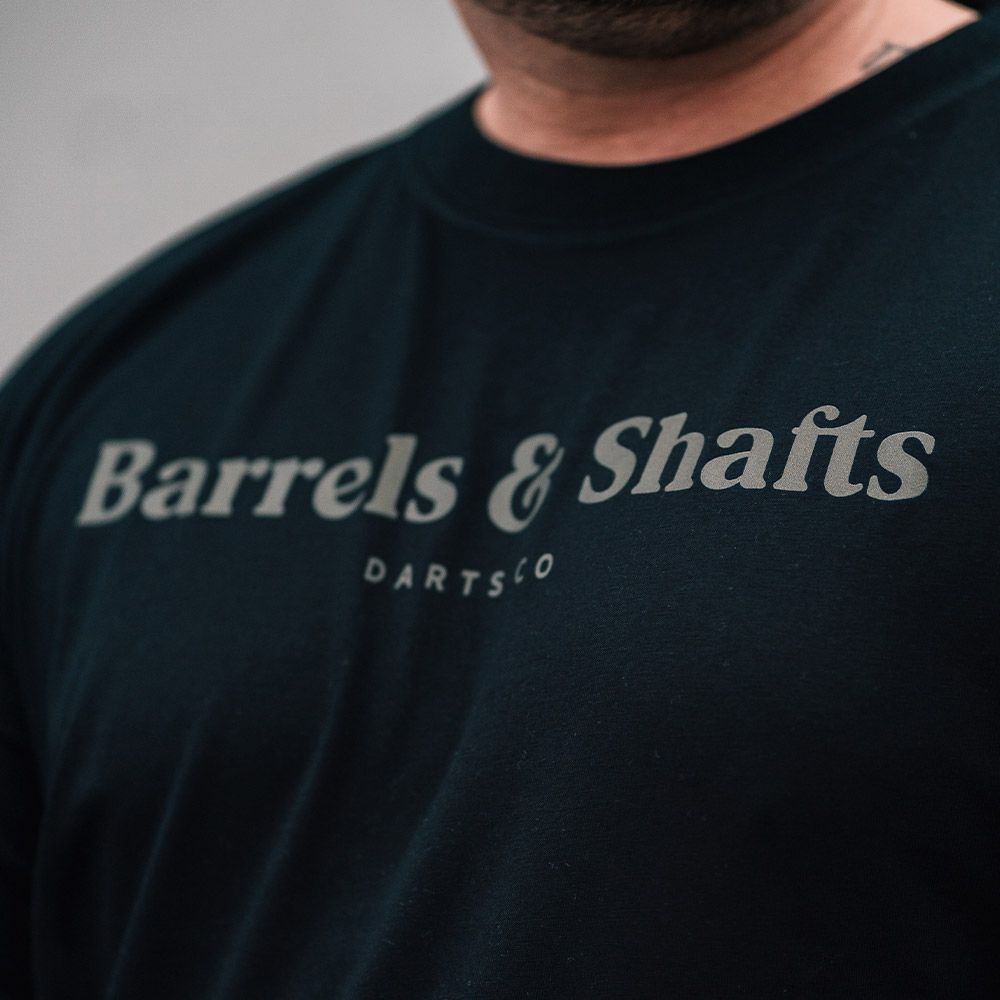 Barrels and Shafts T-Shirt - Black Das Bild zeigt ein schwarzes T-Shirt mit der Aufschrift "Barrels & Shafts". Darunter steht in kleineren Buchstaben "DARTSCO".