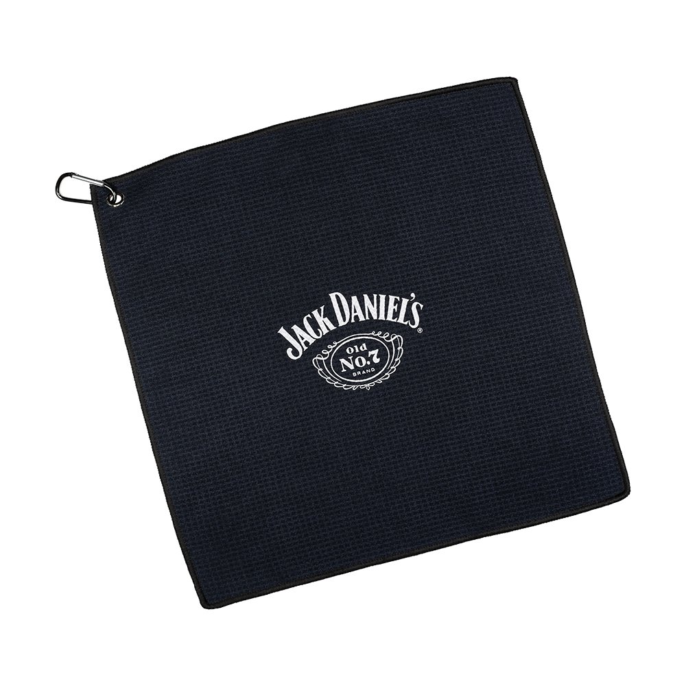 JD7032_Mission_Jack_Daniels_Handtuch_1 Dies ist ein schwarzes Handtuch mit dem weißen Jack Daniel's Logo in der Mitte. In der Ecke befindet sich eine Metallöse mit einem Haken zum Aufhängen.
