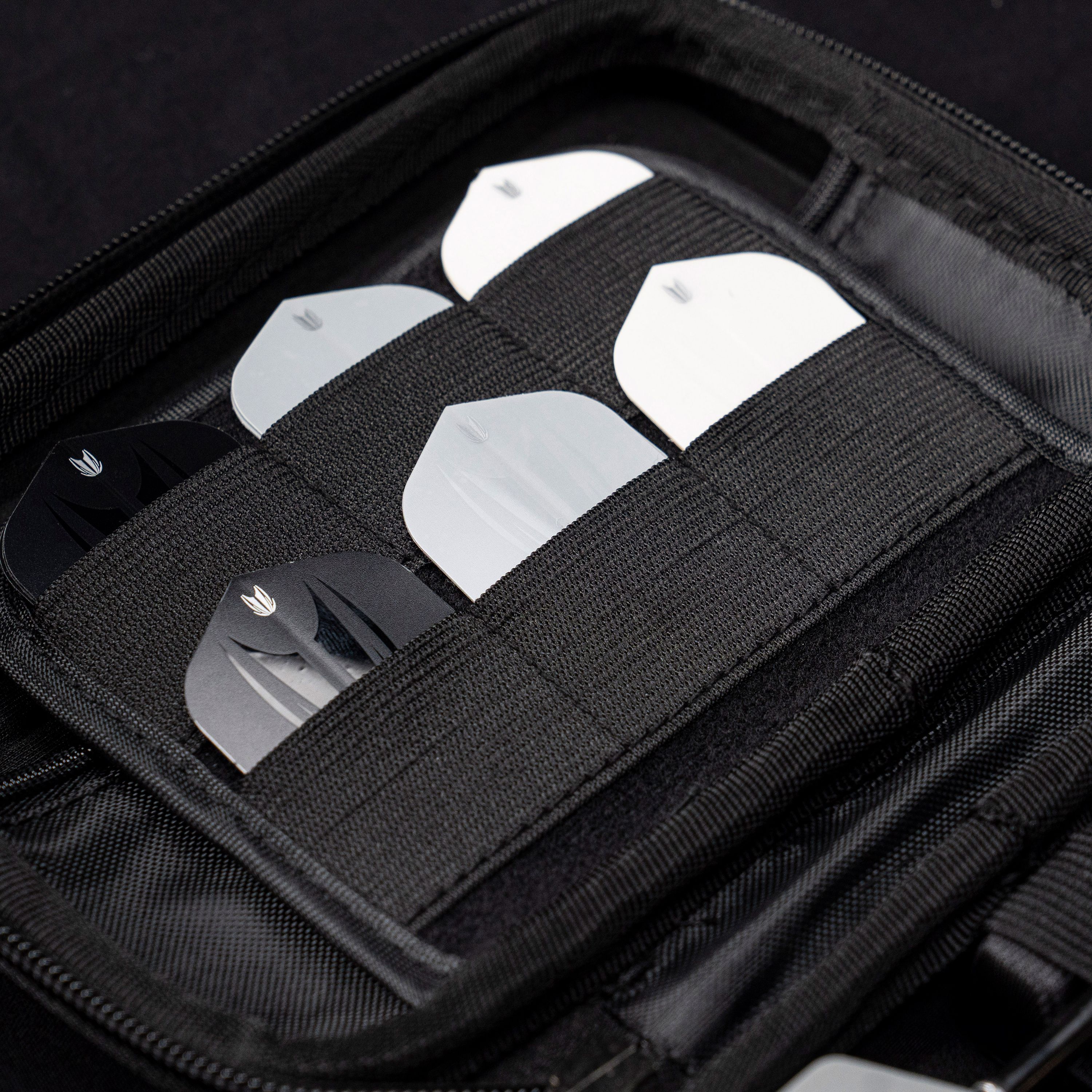 Takoma XL Ghost Series Rob Cross dart case Das Bild zeigt das „Target Takoma Bolide XL Dartcase“, das mehrere Dart-Flights in schwarzen und weißen Farben organisiert aufbewahrt. Die Flights sind sicher in elastischen Halterungen im Inneren des schwarzen Etuis verstaut.