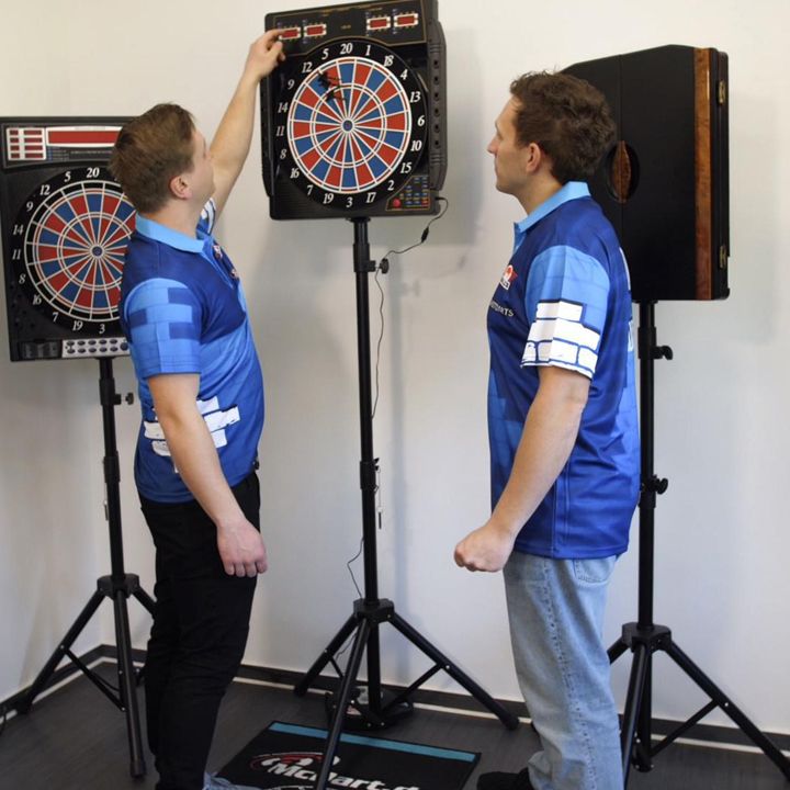 CB50 Zwei Männer in blauen Shirts stehen vor elektronischen Dartscheiben. Einer der Männer nimmt einen Dartpfeil aus der Dartscheibe.