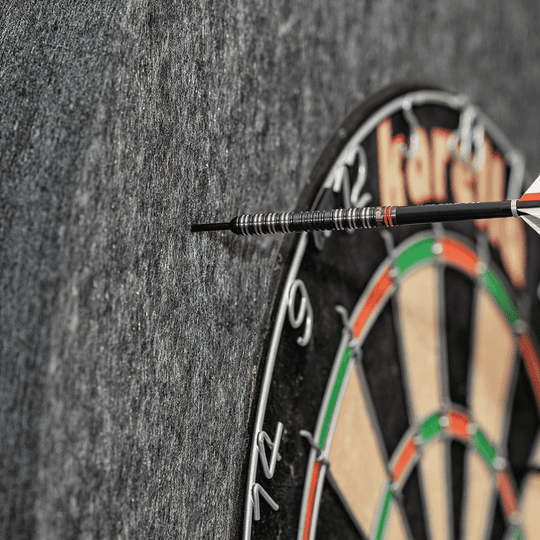 811501_Karella_Schallschutz_f-r_Steeldartboards_5 Das Bild zeigt ein Steeldartboard mit dem Schallschutz Karella und integriertem Surround Auffangring. Ein Dartpfeil steckt in dem schallschluckenden Auffangring neben der Dartscheibe.